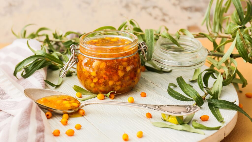 Klaaspurgis siirupjas astelpajusegu, kõrval lusikas ja leheoksad — kaanefoto artiklile astelpaju kuumustundlikkusest.